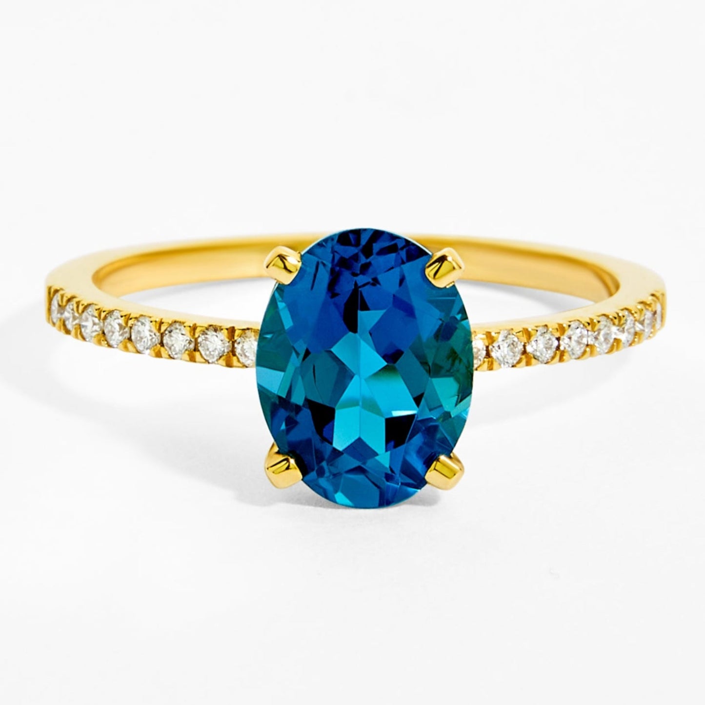 Gold ring with a blue gemstone and diamond-studded band on a white background