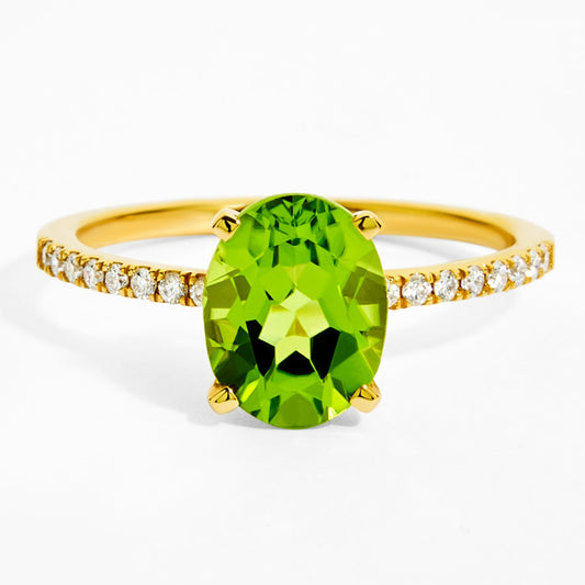 Gold ring with a green gemstone and diamond-studded band on a white background